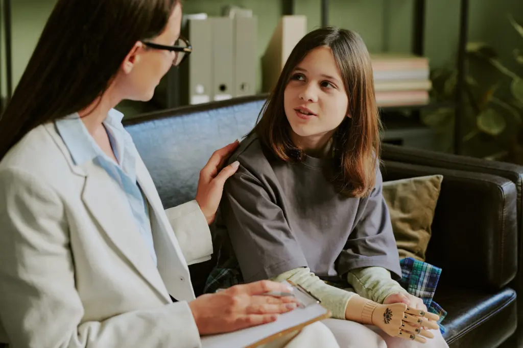 Teenage girl with prosthetic limb engaging with therapist on sofa focusing on recovery and future steps Together discussing personal progress in friendly environment